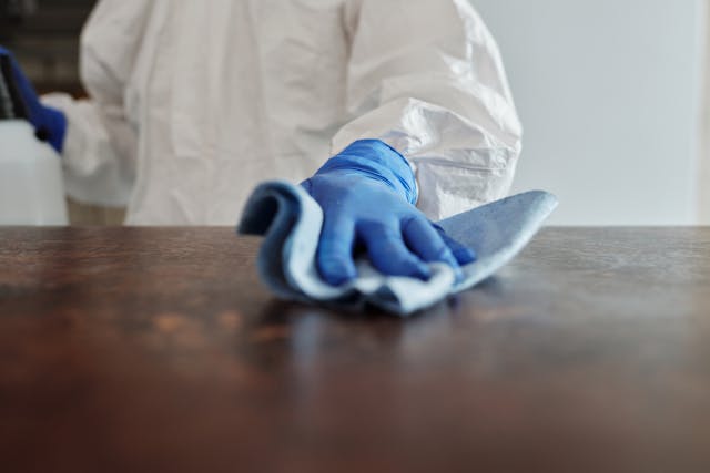 person wearing a white cleaning suit and medical gloves wiping down a table, demonstrating how to prepare for pest control